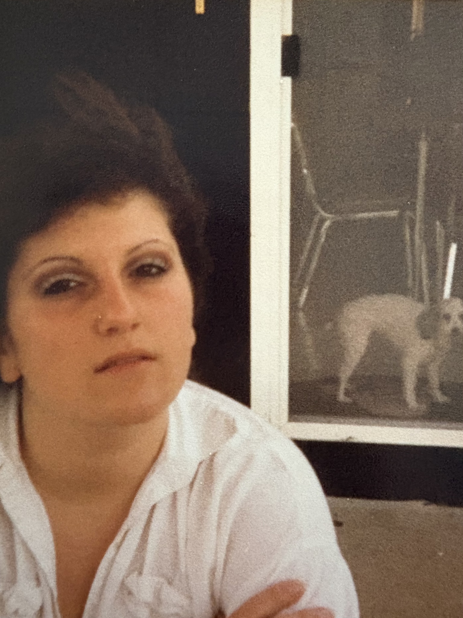Rhonda sitting with folded arms in front of a glass door, a small whit