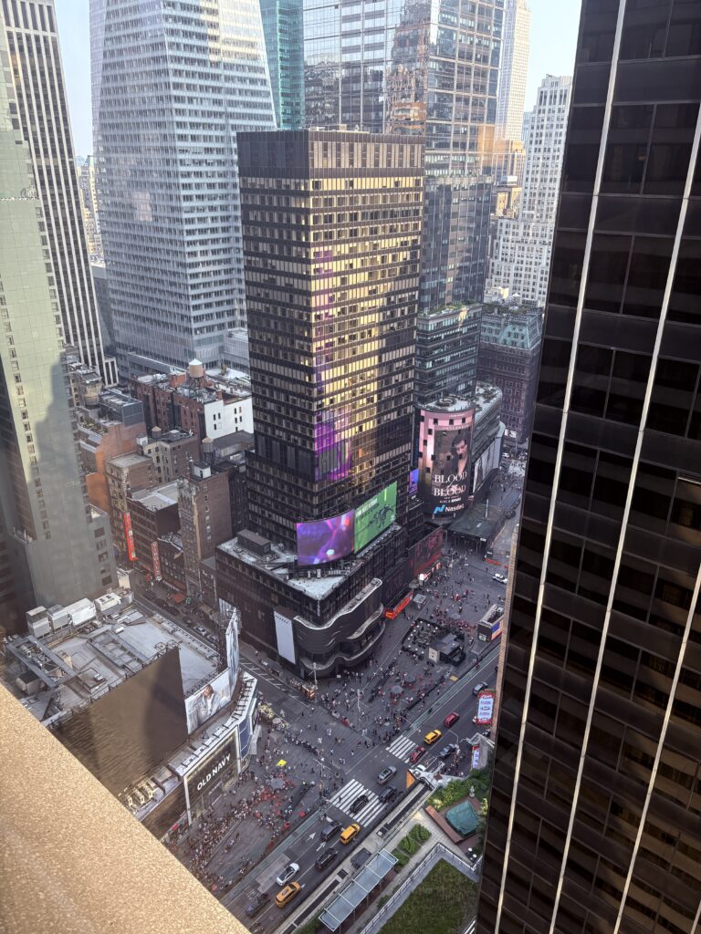 "View of Times Square from hotel room window in New York City, with lights and billboards visible