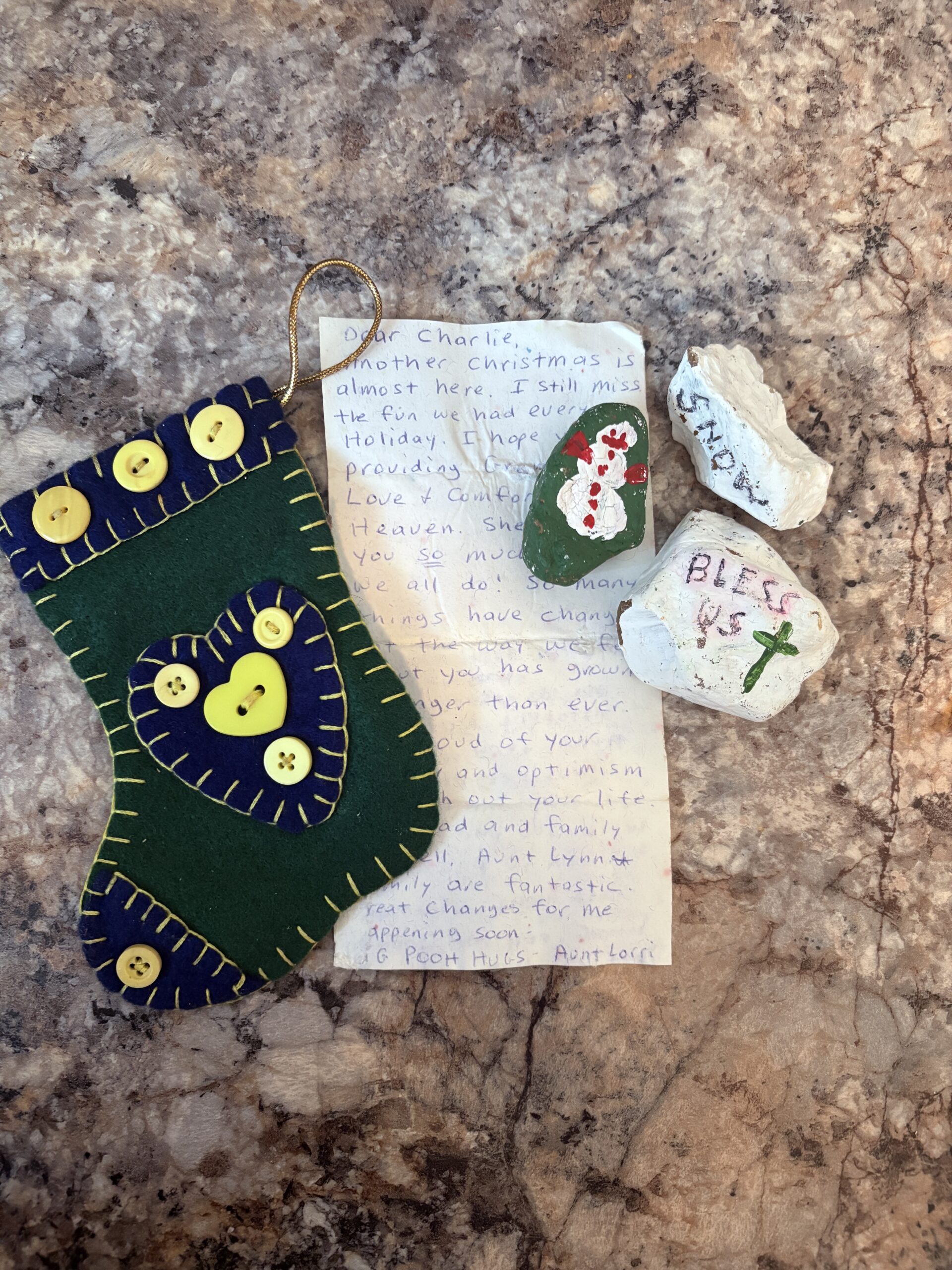 Handmade felt Christmas stocking with buttons, painted blessing stones, and a handwritten letter on a marble background
