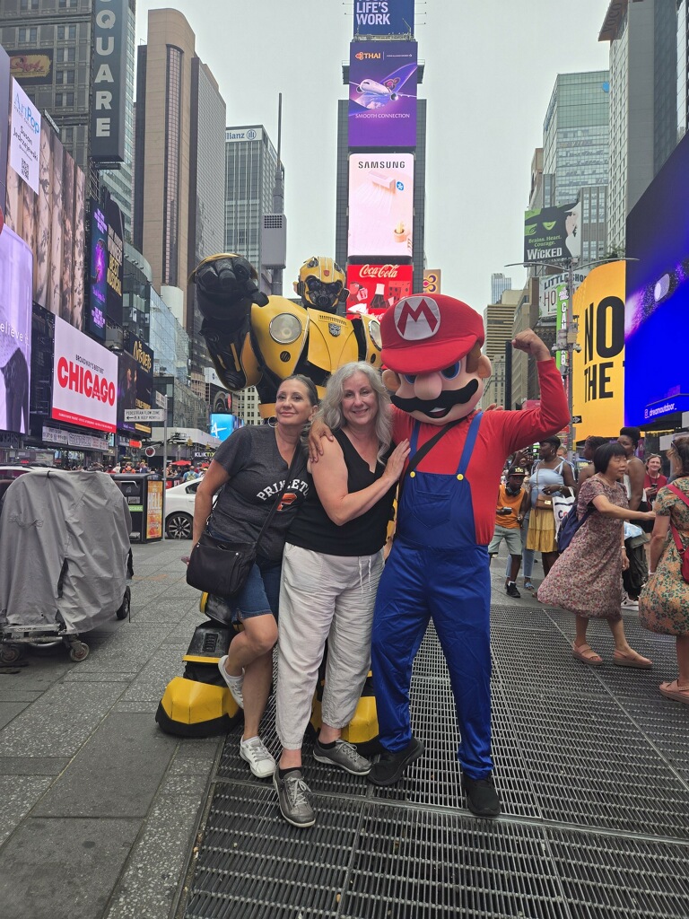 Lisa and Cora posing with street performers dressed as Bumblebee and Mario in Times Square, New York City.