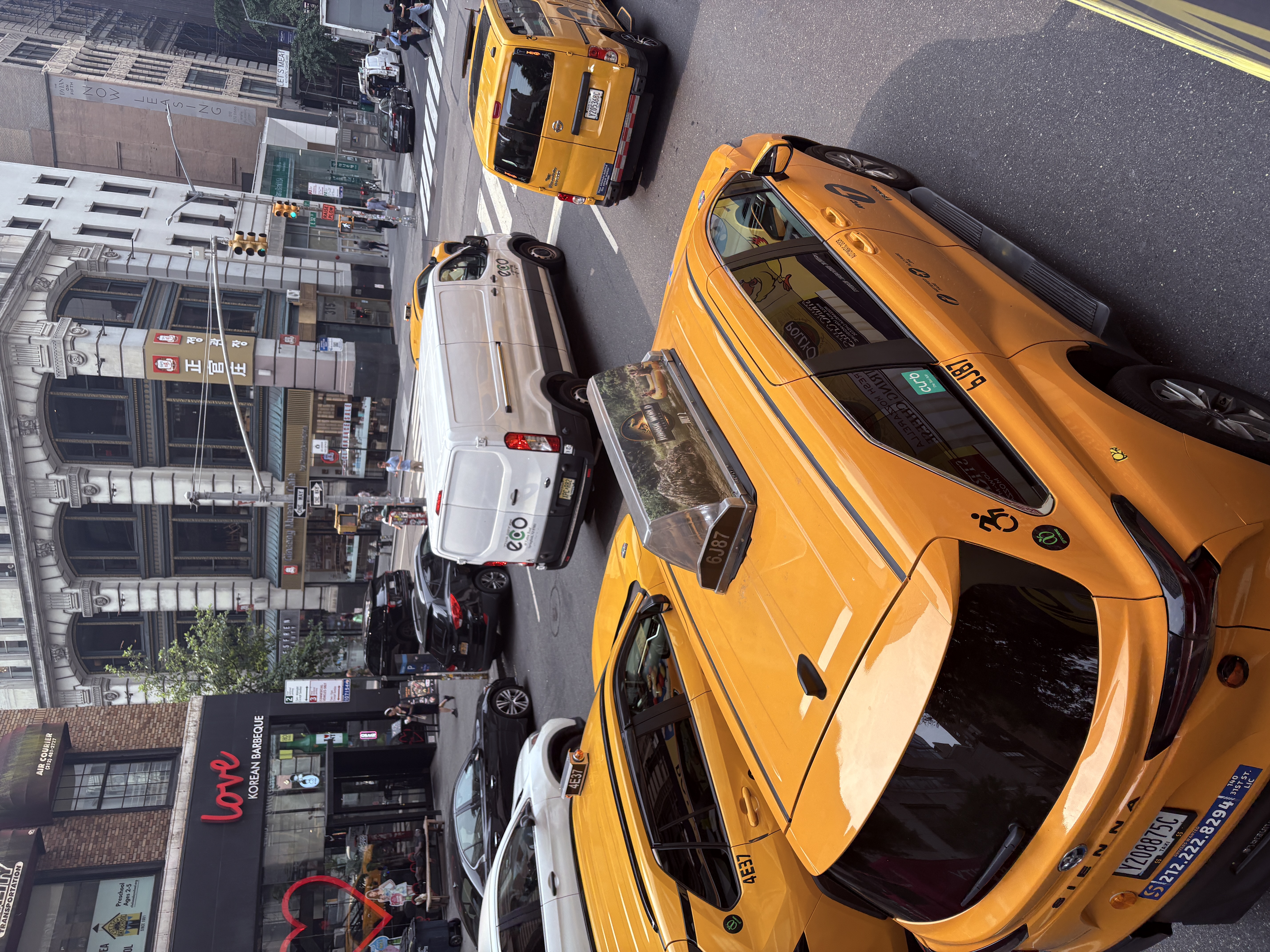 Yellow taxis and traffic on a busy New York City street, viewed from above.