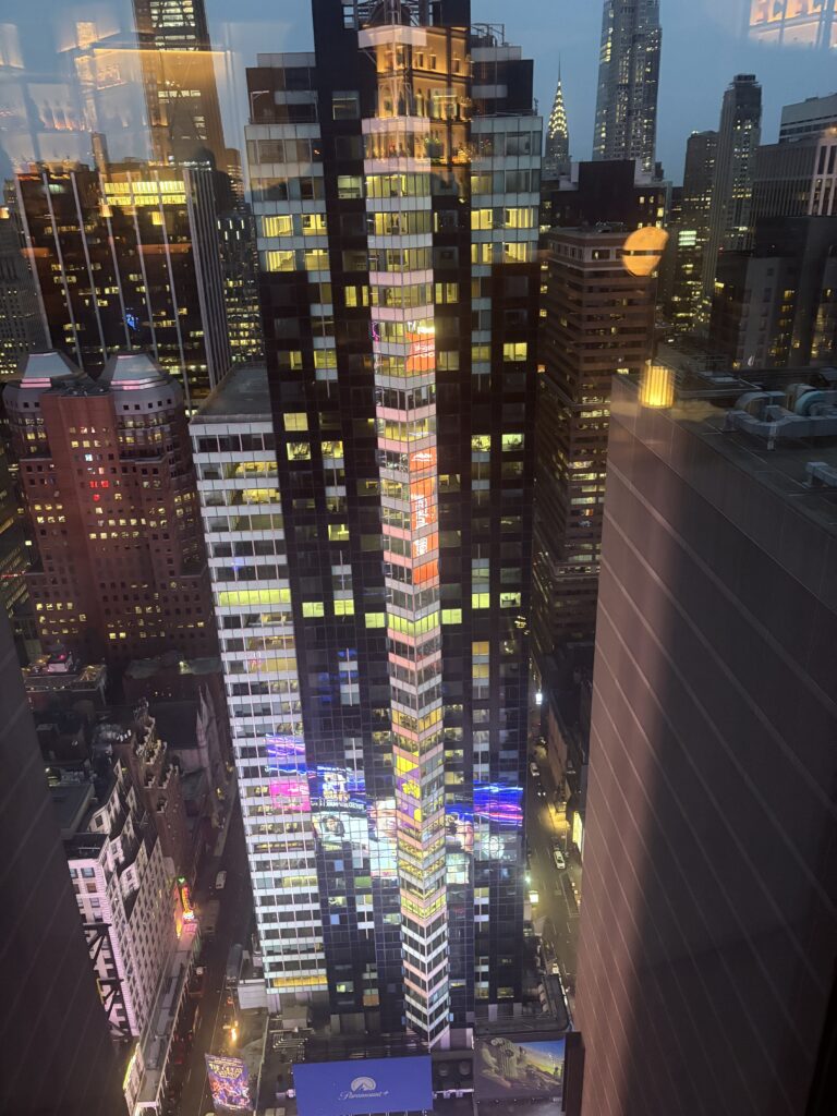 Aerial view of New York City skyscrapers at dusk, with colorful lights beginning to glow.