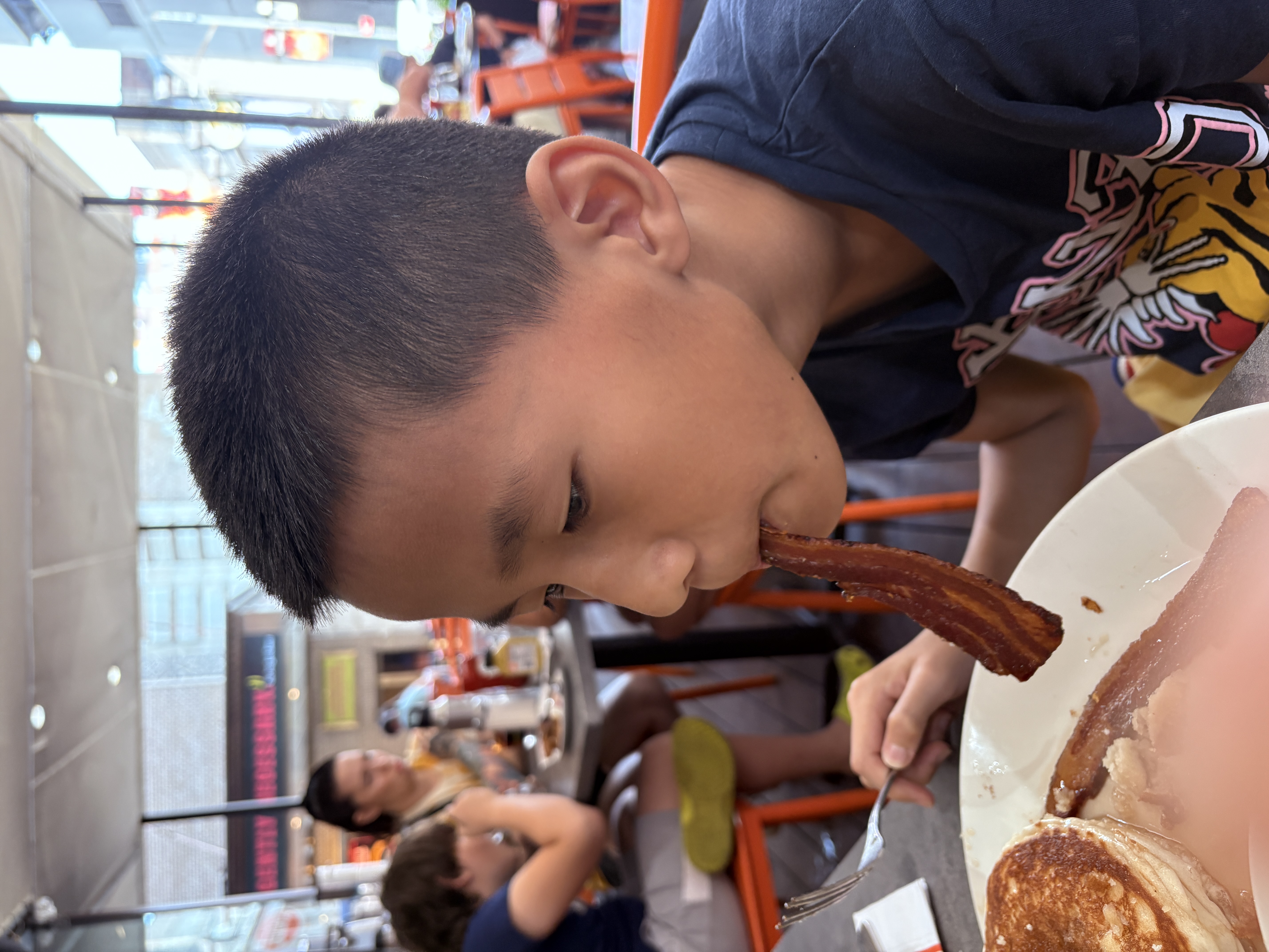 Victor holding up a strip of bacon playfully during breakfast at Junior’s in New York.