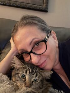 Lisa sitting on a couch, smiling gently while holding her cat Mia close, wearing glasses in a relaxed home setting
